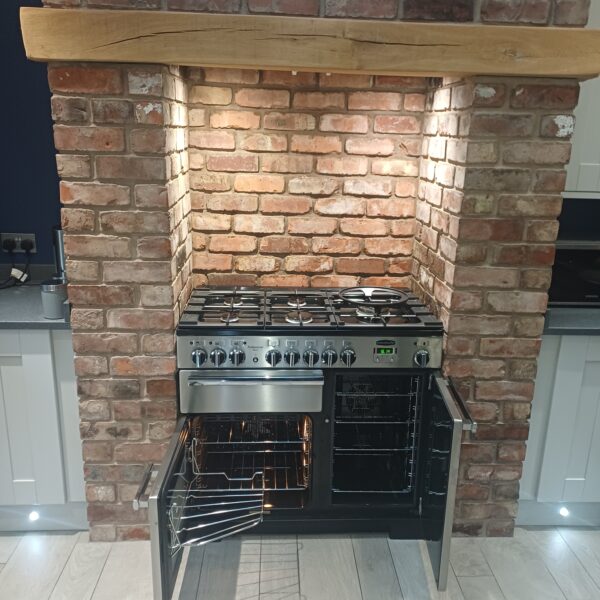 Full view of the cleaned Rangemaster Professional range cooker with open ovens beneath a timber mantel and brick surround in Hopwas.